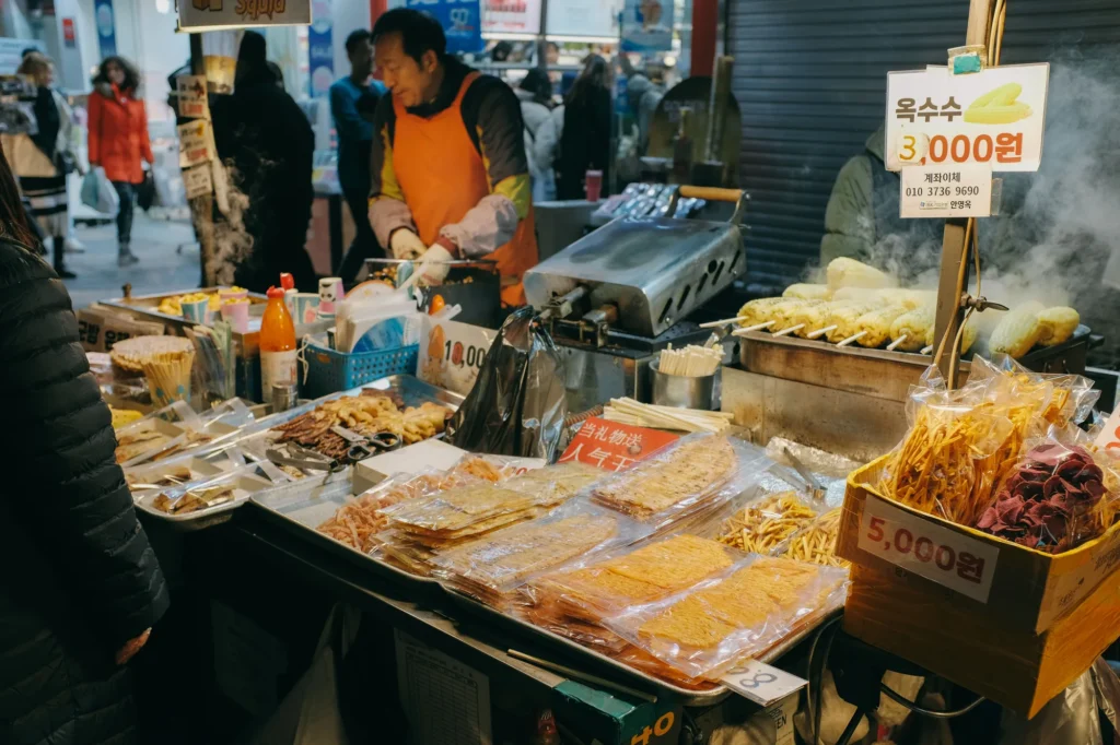 Stand de street food à Séoul avec épis de maïs grillés et snacks séchés, prix affichés en wons