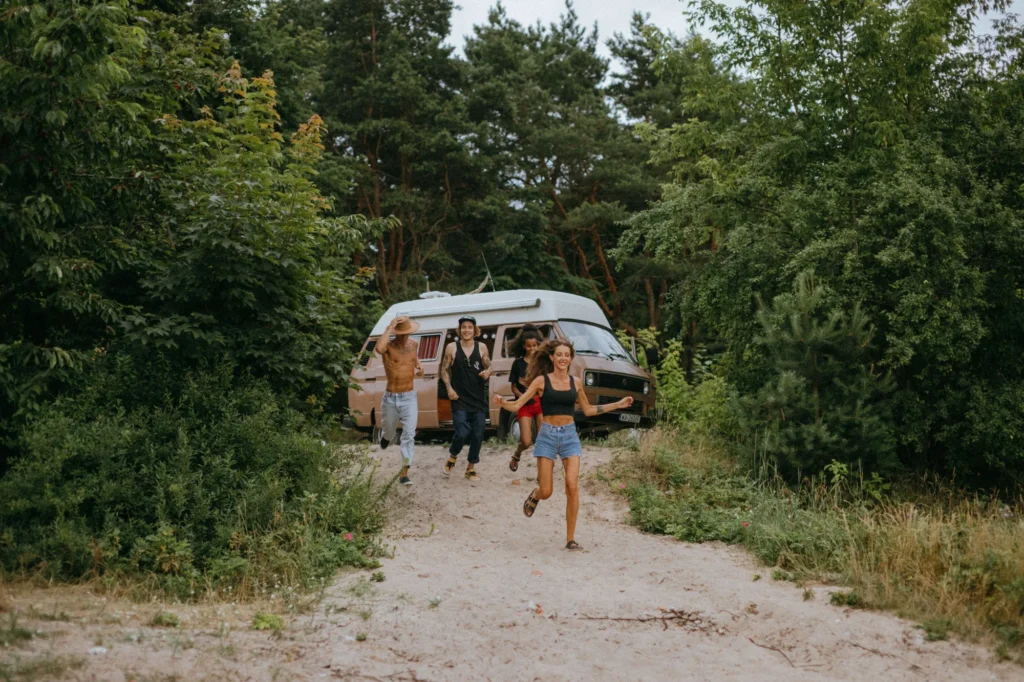 Voyage entre amis : un groupe d'amis court joyeusement devant un van dans la forêt