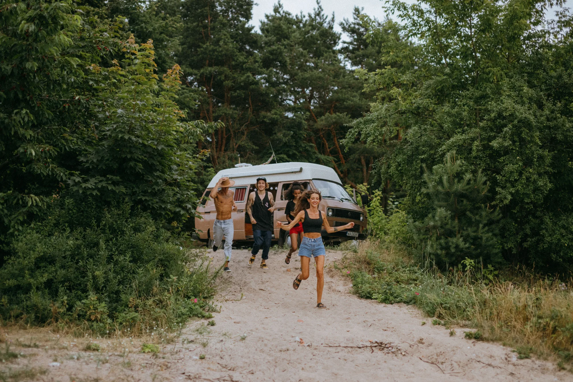 Voyage entre amis : un groupe d'amis court joyeusement devant un van dans la forêt