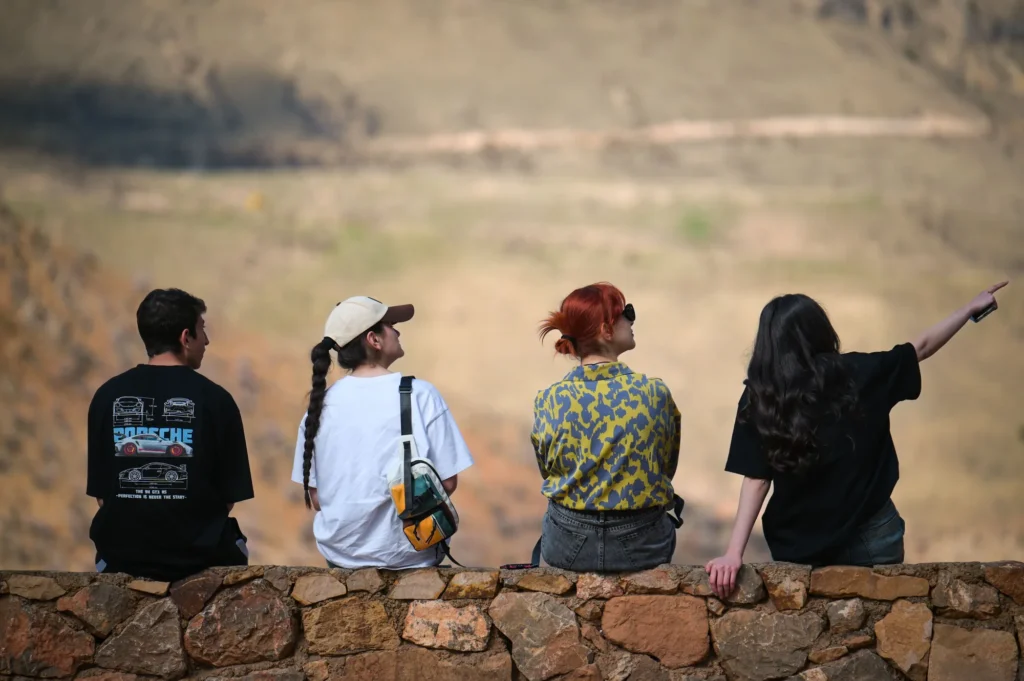 Quatre amis assis sur un muret de pierre devant un paysage de montagne